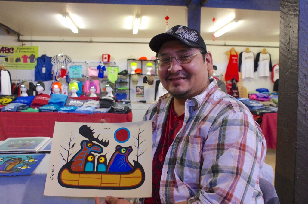 Gull Bay artist Kevin Belmore with his animal protest painting that features a group of animals leaving in a canoe over man’s destruction of the environment.  Photo by Rick Garrick